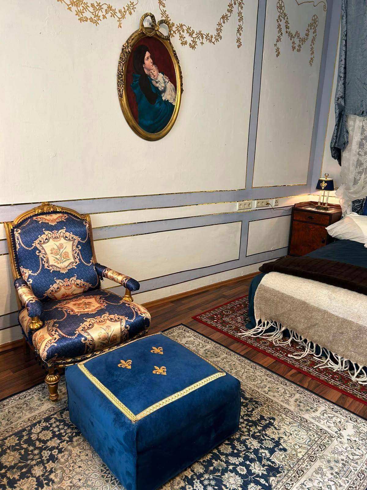 Opulentes Schlafzimmer mit blauem Samtsessel, passendem Hocker und klassischer Wandgestaltung.