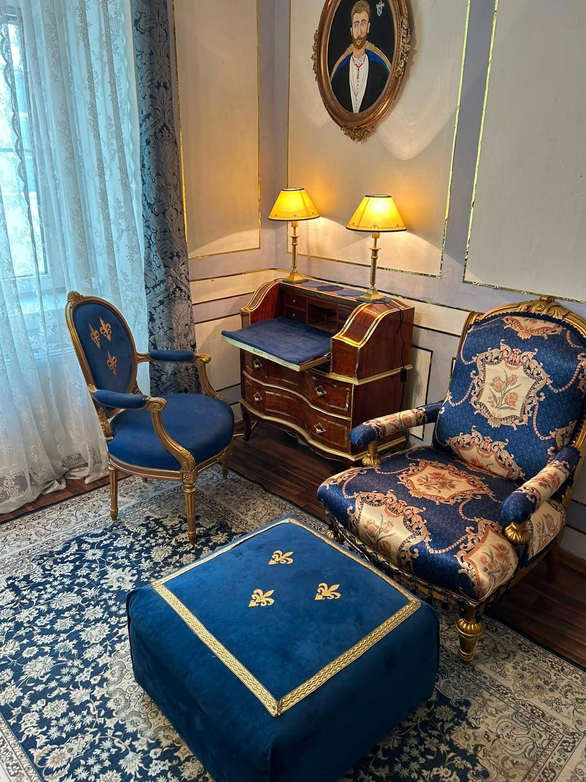 Helles Wohnzimmer mit eleganten blauen Möbeln, antikem Schreibtisch und Vorhängen am Fenster.