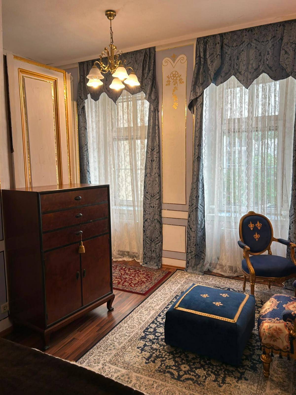 Geräumiges Zimmer mit zwei Fenstern, Kronleuchter und antiken Möbeln in königlichem Stil.