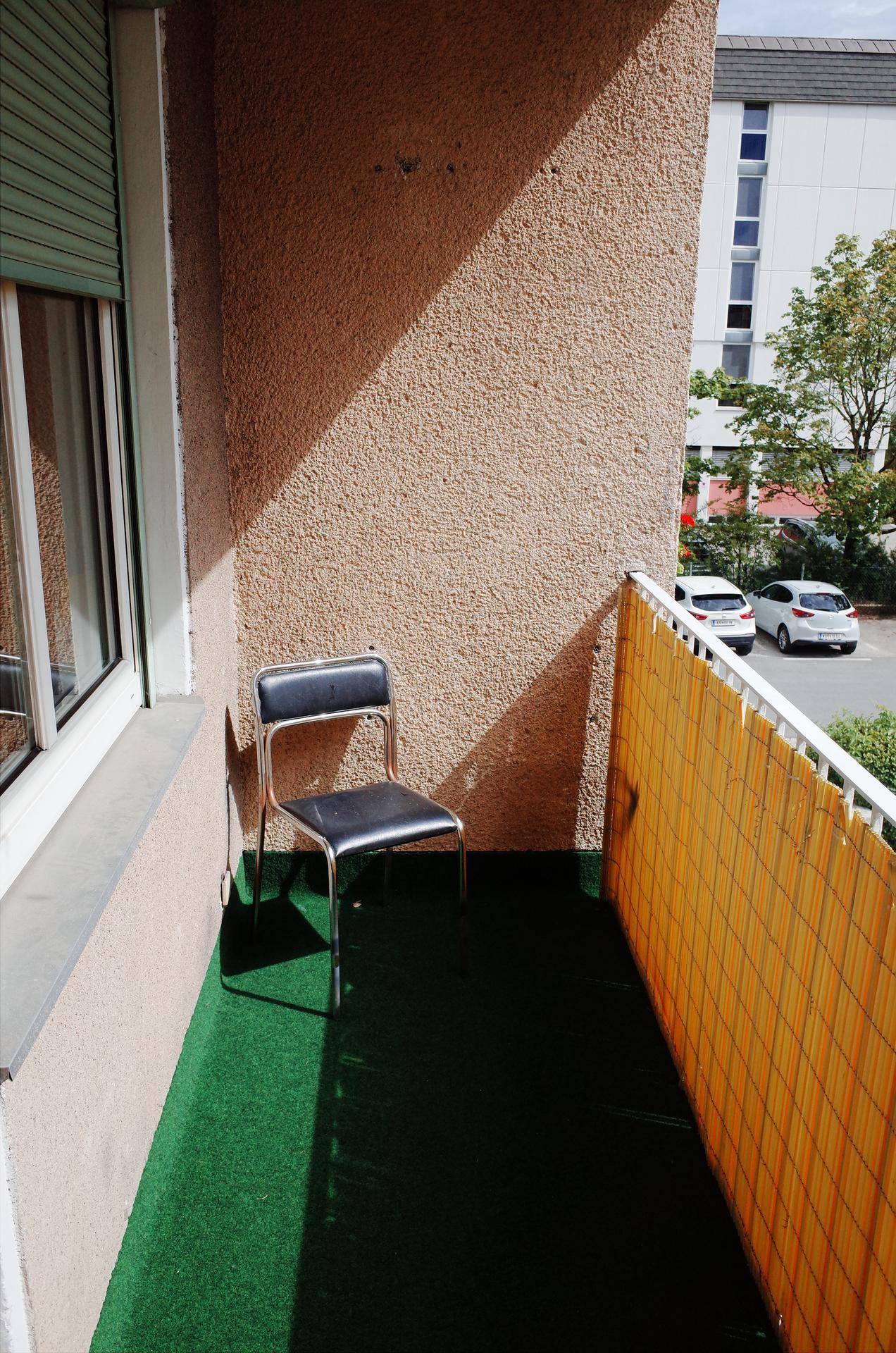 Kleiner Balkon mit Kunstrasen und einem Stuhl, bietet Blick auf den Außenbereich.