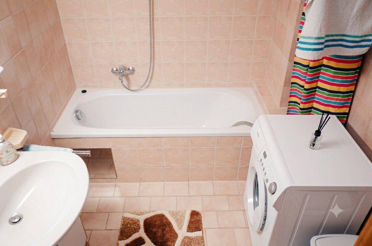 Badezimmer mit Badewanne, Waschbecken und einer Waschmaschine, gefliest in Pastellfarben.