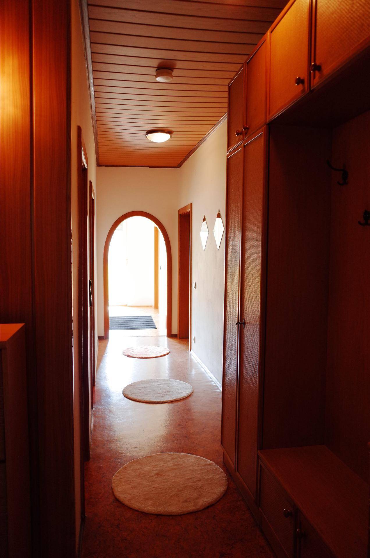 Langer Flur mit Holzvertäfelung an Decke und Wänden, ausgelegt mit runden Teppichen.