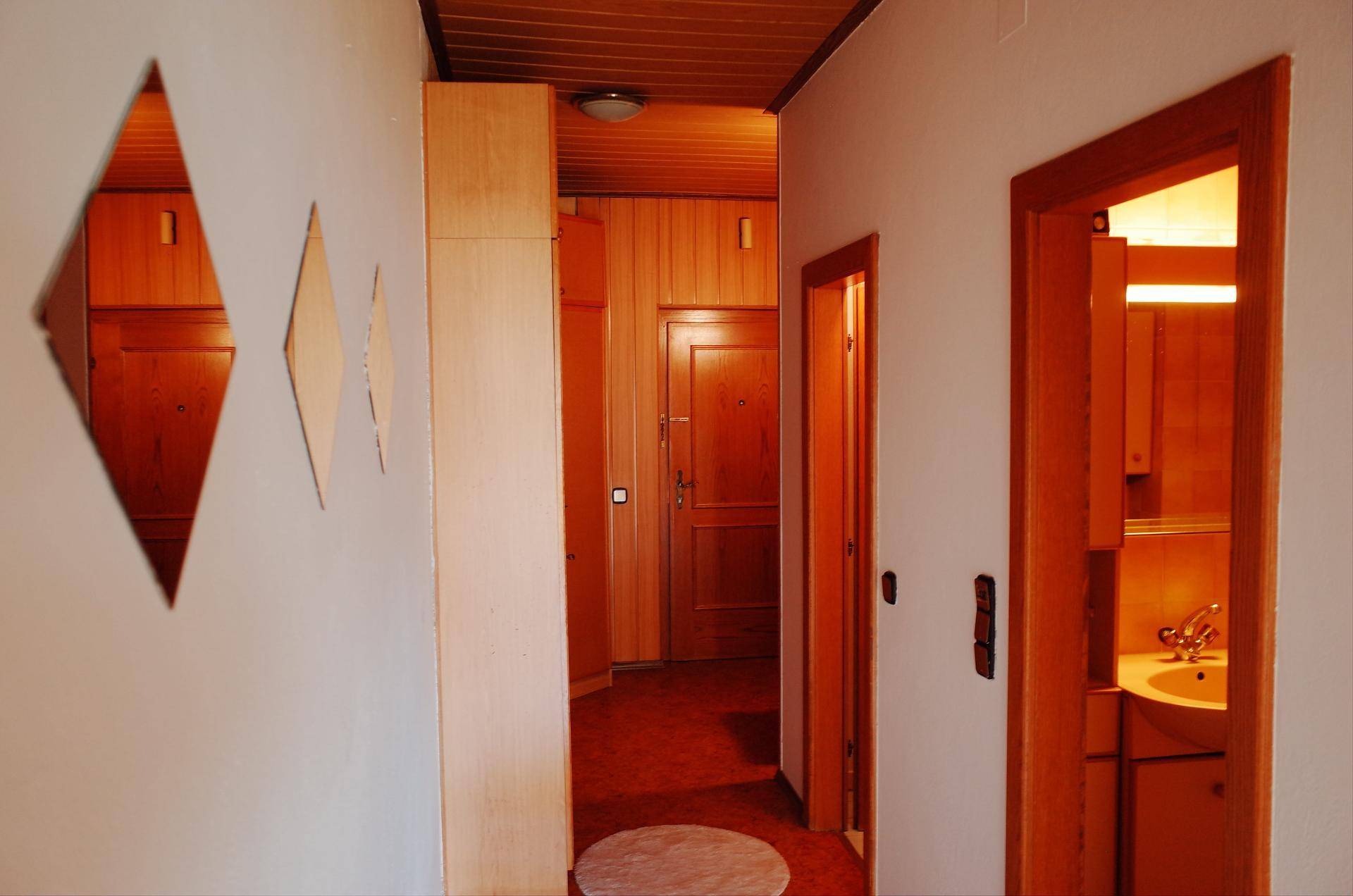 Flur mit Holzvertäfelung, dekorativen Spiegeln und Blick in ein Badezimmer.