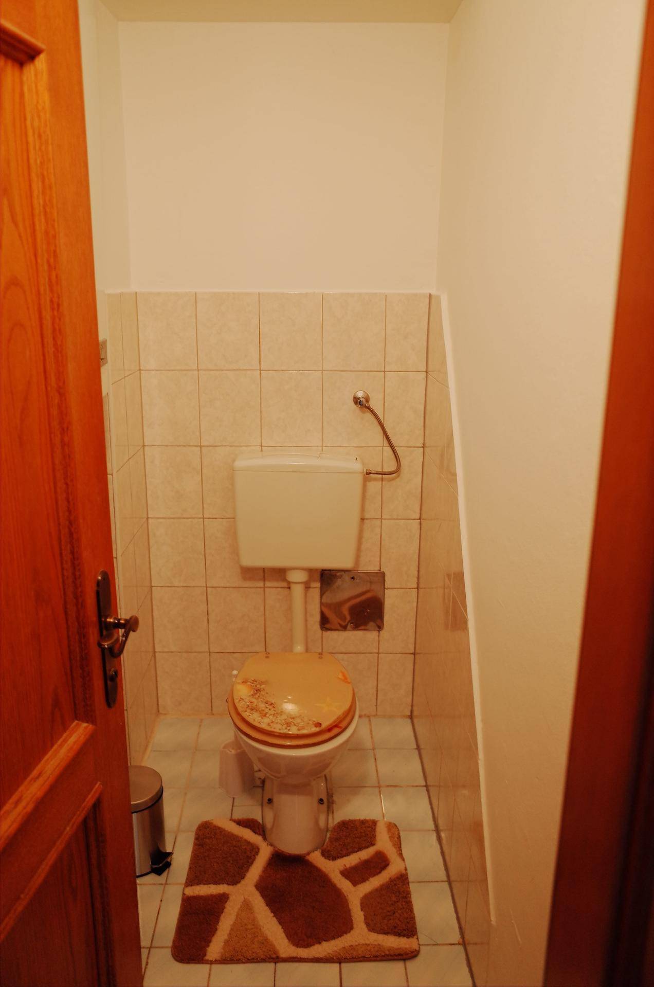 Kleines Gäste-WC mit Toilette und hellen Fliesen an Wänden und Boden.