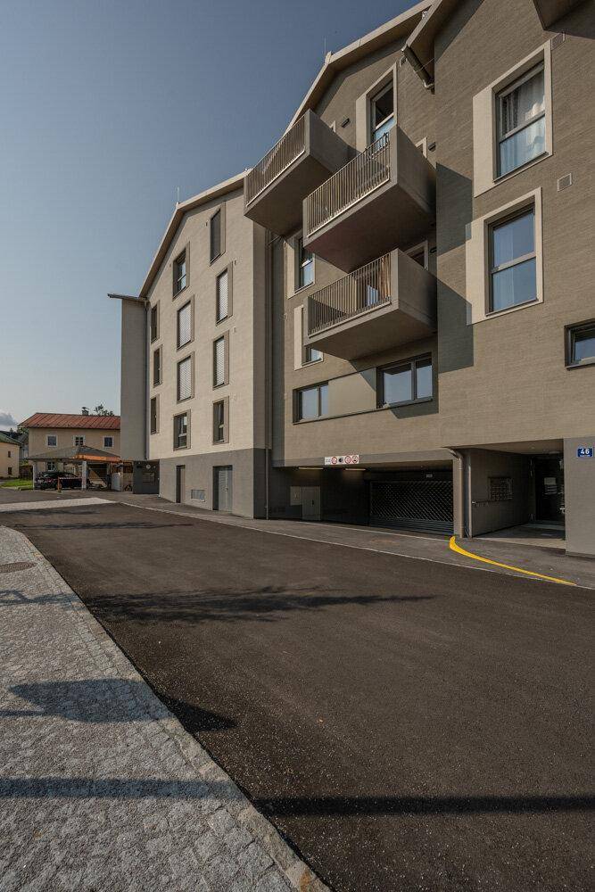 Moderne Wohnhausfassade mit Balkonen und Zufahrt zur Tiefgarage, bei Tageslicht.