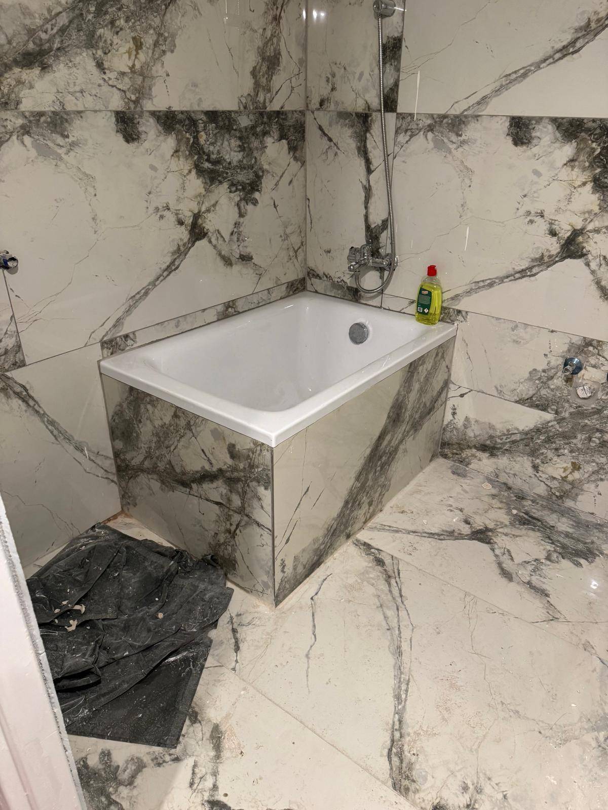 Badezimmer mit eingebauter Badewanne und eleganten Marmor-Effekt-Fliesen an Wänden und Boden.