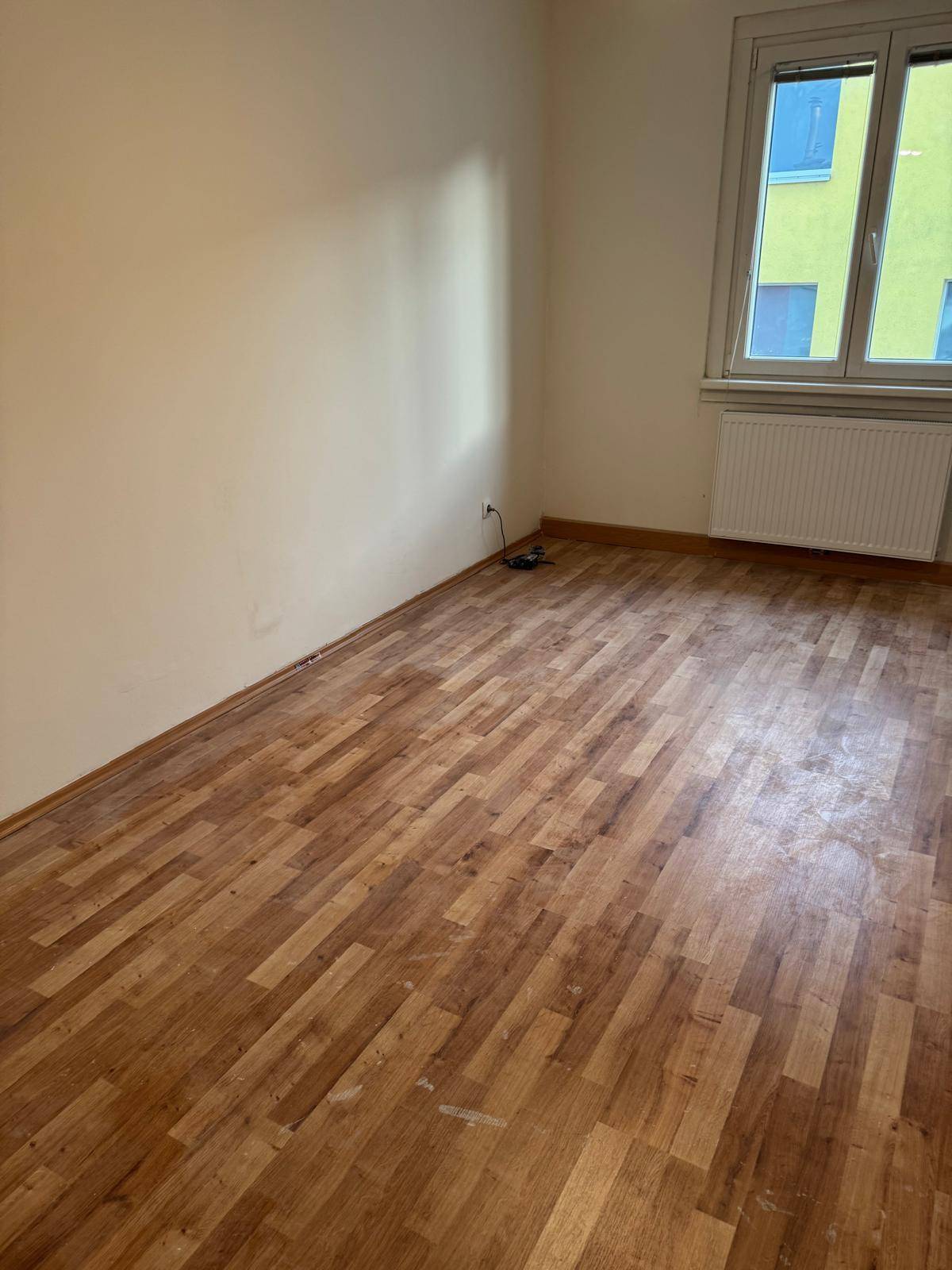 Heller Raum mit Holzboden und Fenster, das Tageslicht hereinlässt, bereit zur Gestaltung.