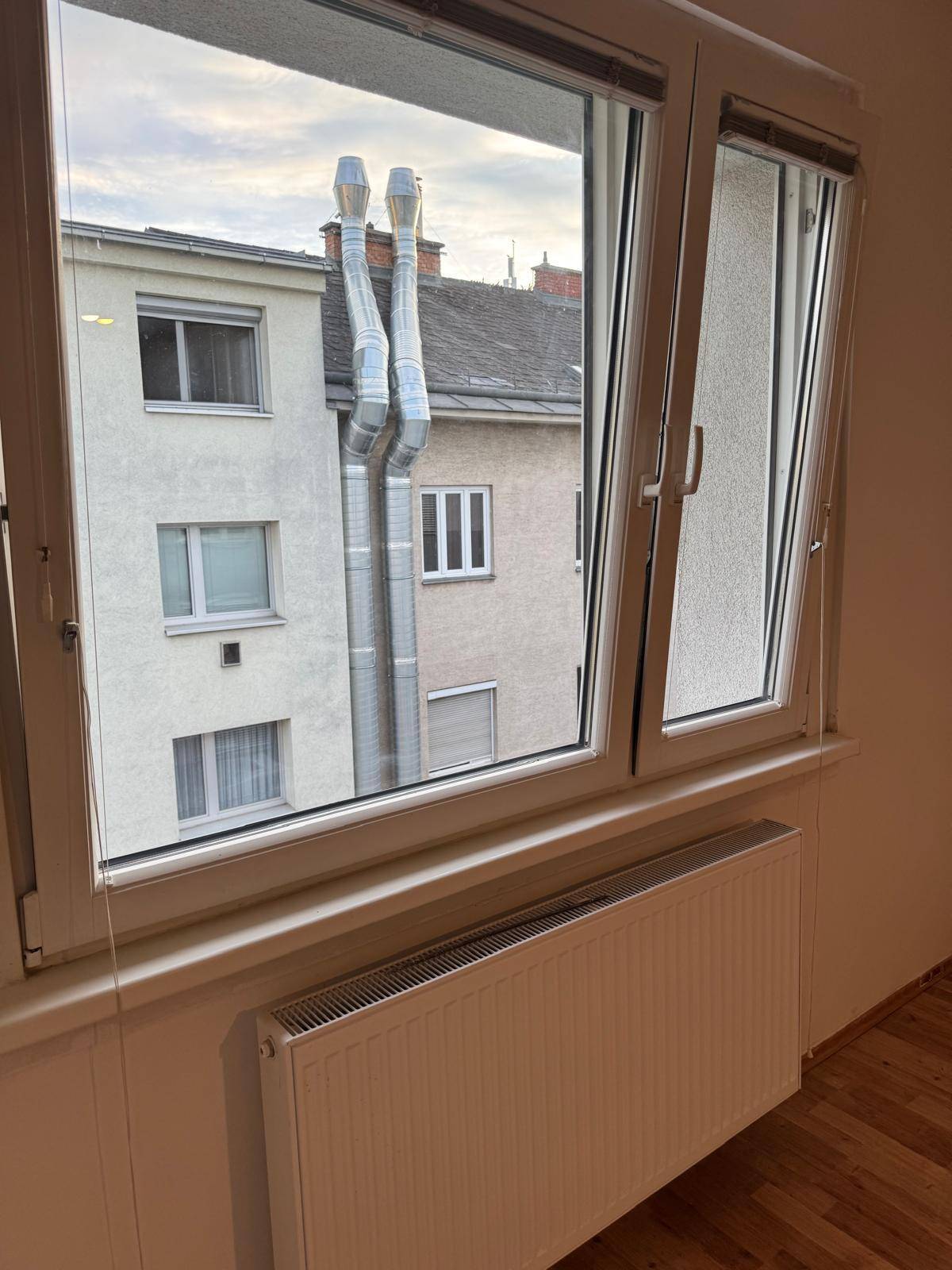 Fenster mit Heizkörper und Blick auf die umliegenden Gebäude mit großen Schornsteinen.