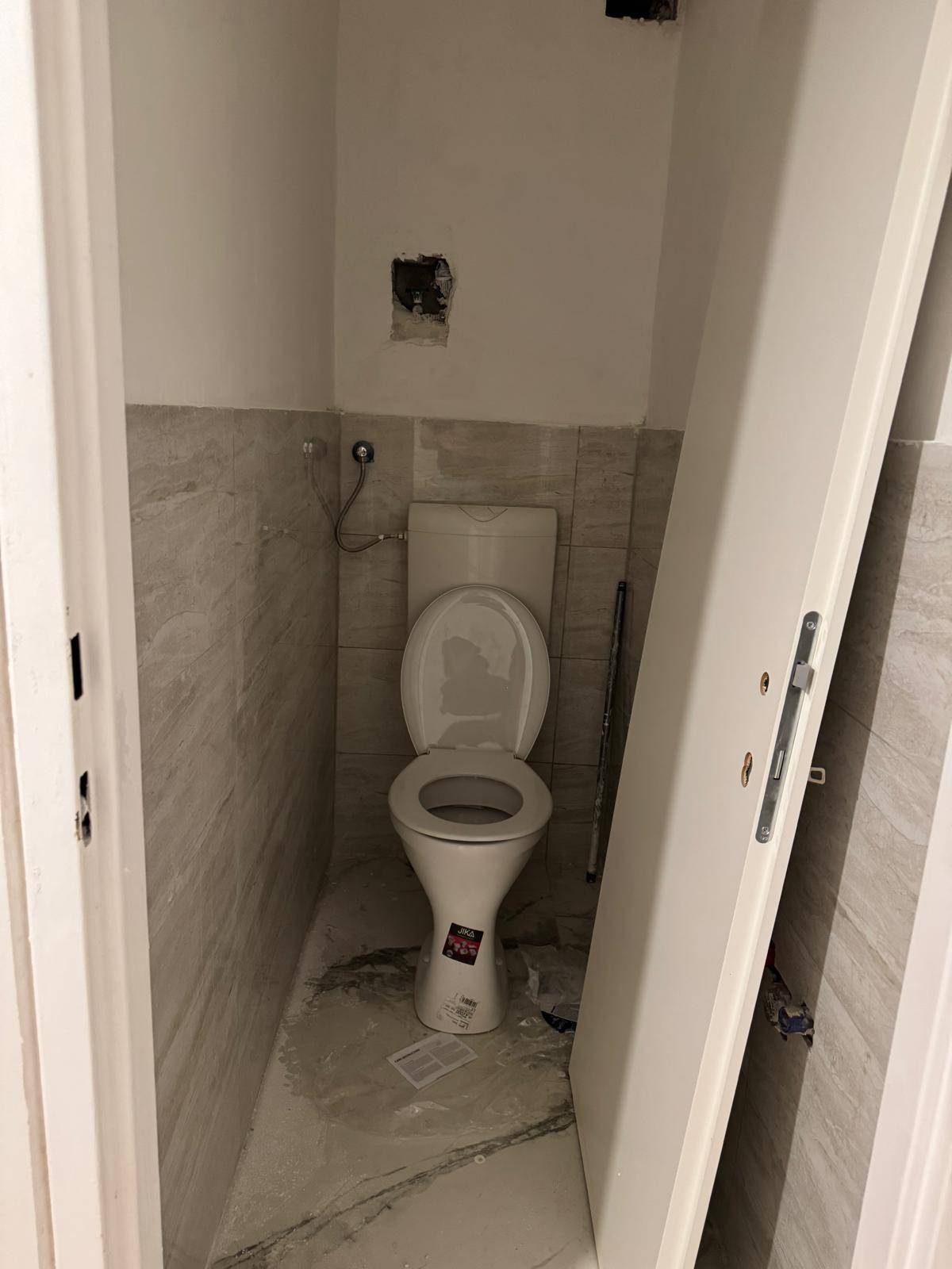 Kleines WC mit Toilette und gefliesten Wänden, noch im Renovierungs- oder Bauzustand.