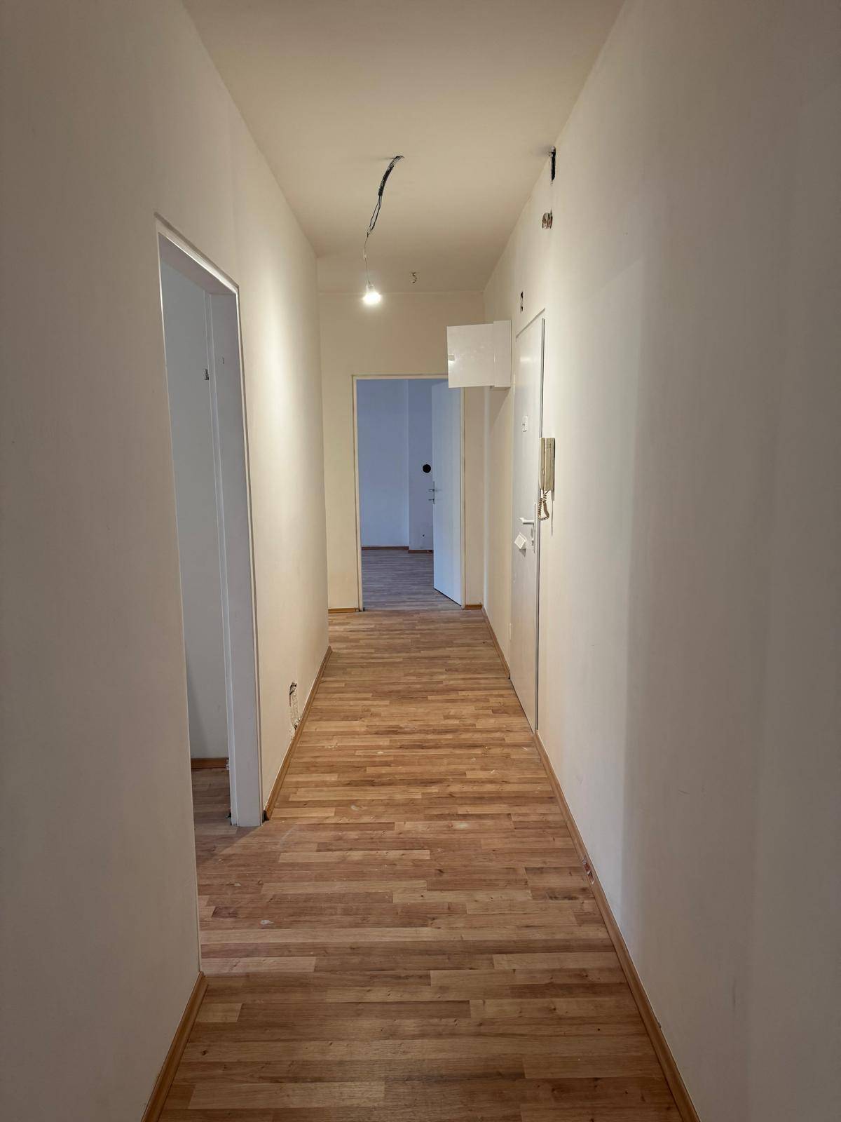 Langer, heller Flur mit Holzboden und weißen Wänden, der zu verschiedenen Zimmern führt.