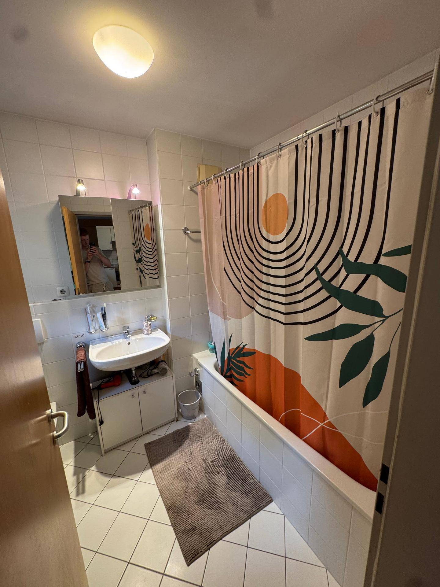 Badezimmer mit weißen Fliesen, Badewanne, Waschbecken und Spiegelschrank.