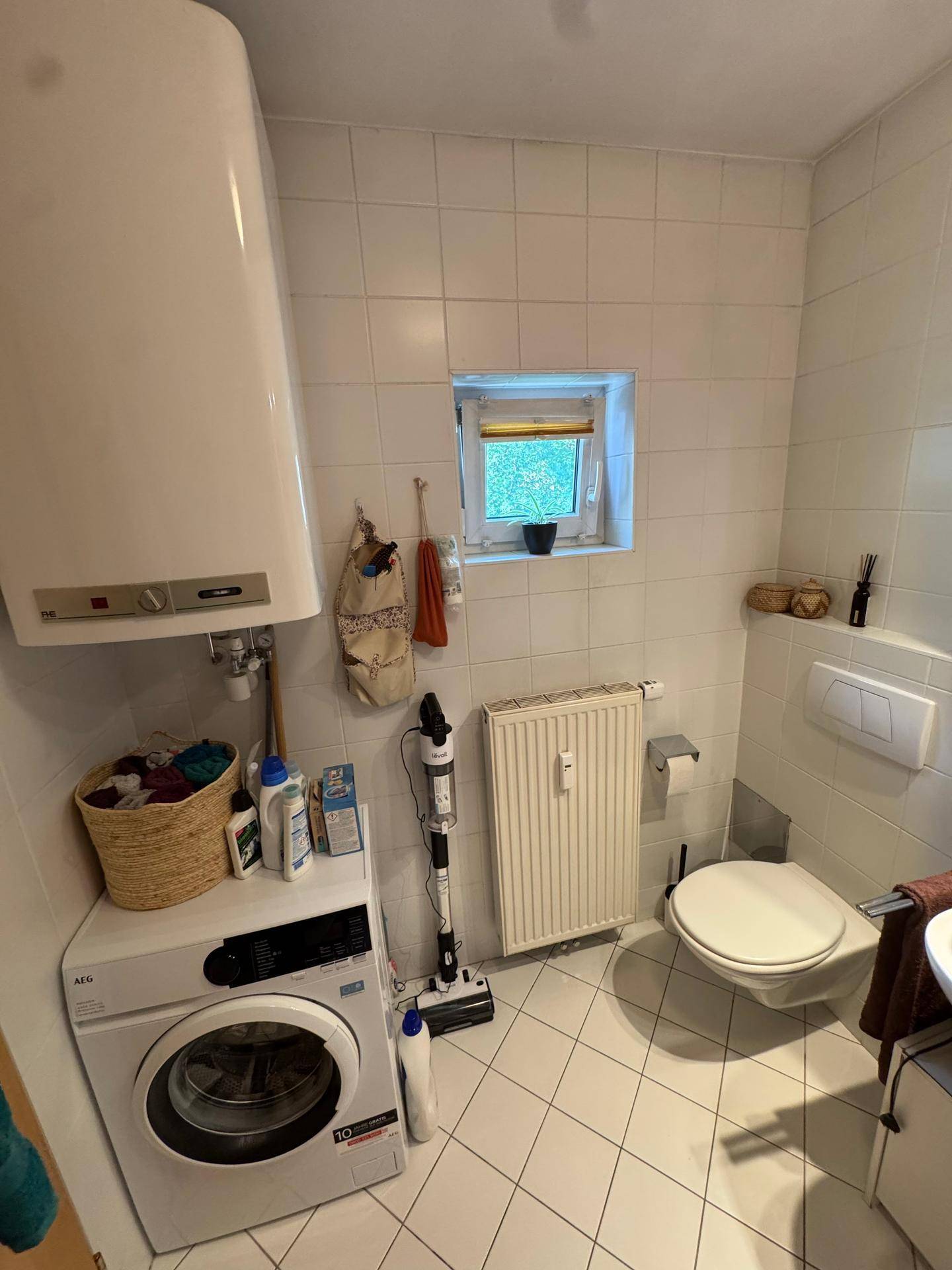WC mit Waschmaschine, Warmwasserboiler und kleinem Fenster.