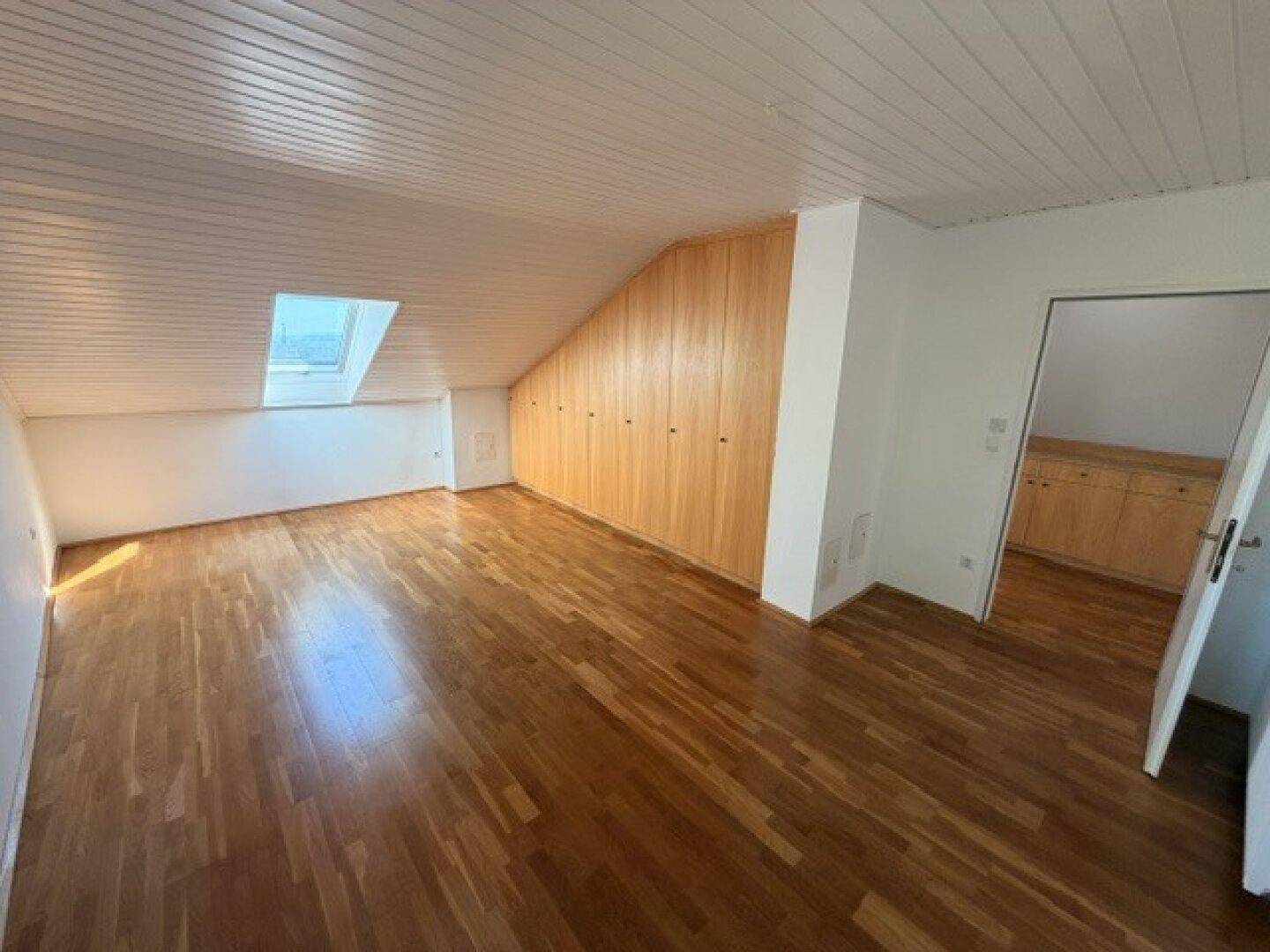 Heller Dachraum mit Holzfußboden, Dachschräge und eingebauten Holzschränken.