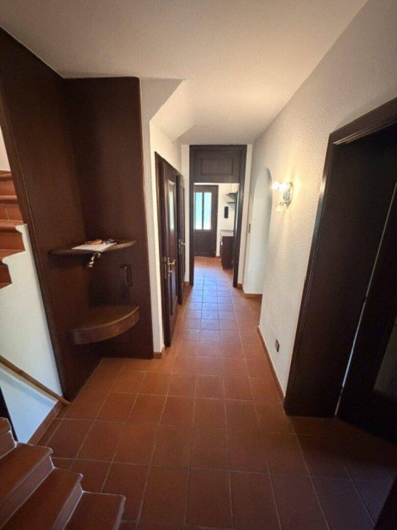 Langer Flur mit Terrakottafliesen, dunklen Holztüren und einer Holztreppe.