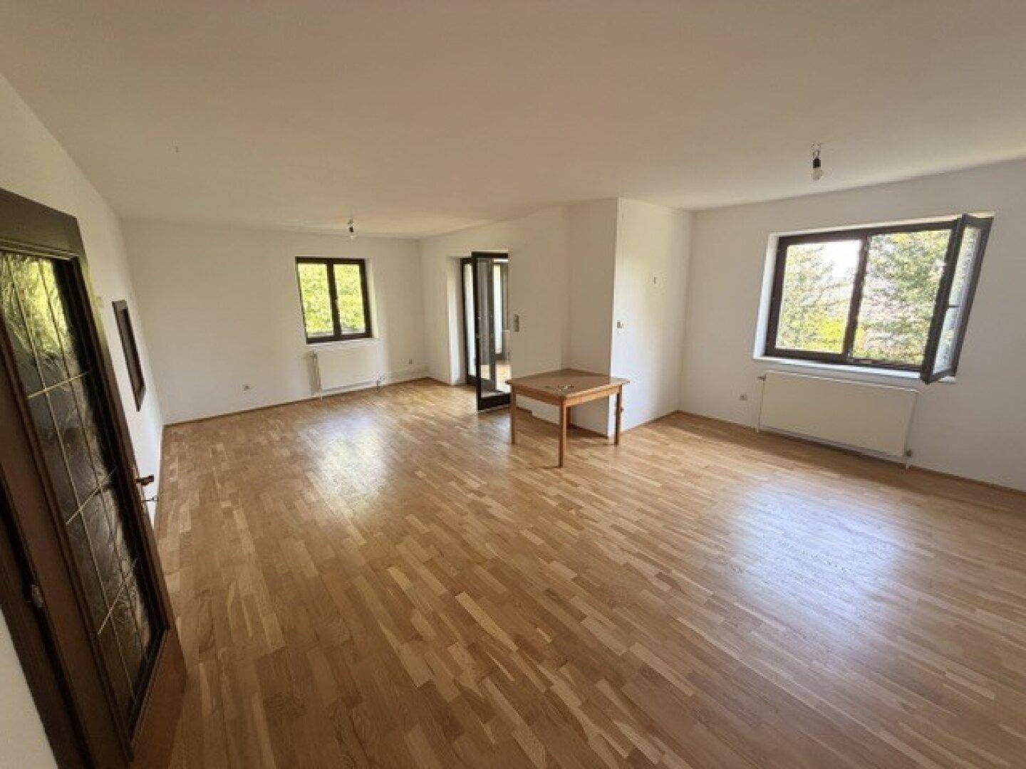 Helles Wohnzimmer mit Holzfußboden und mehreren Fenstern, die viel Tageslicht hereinlassen.