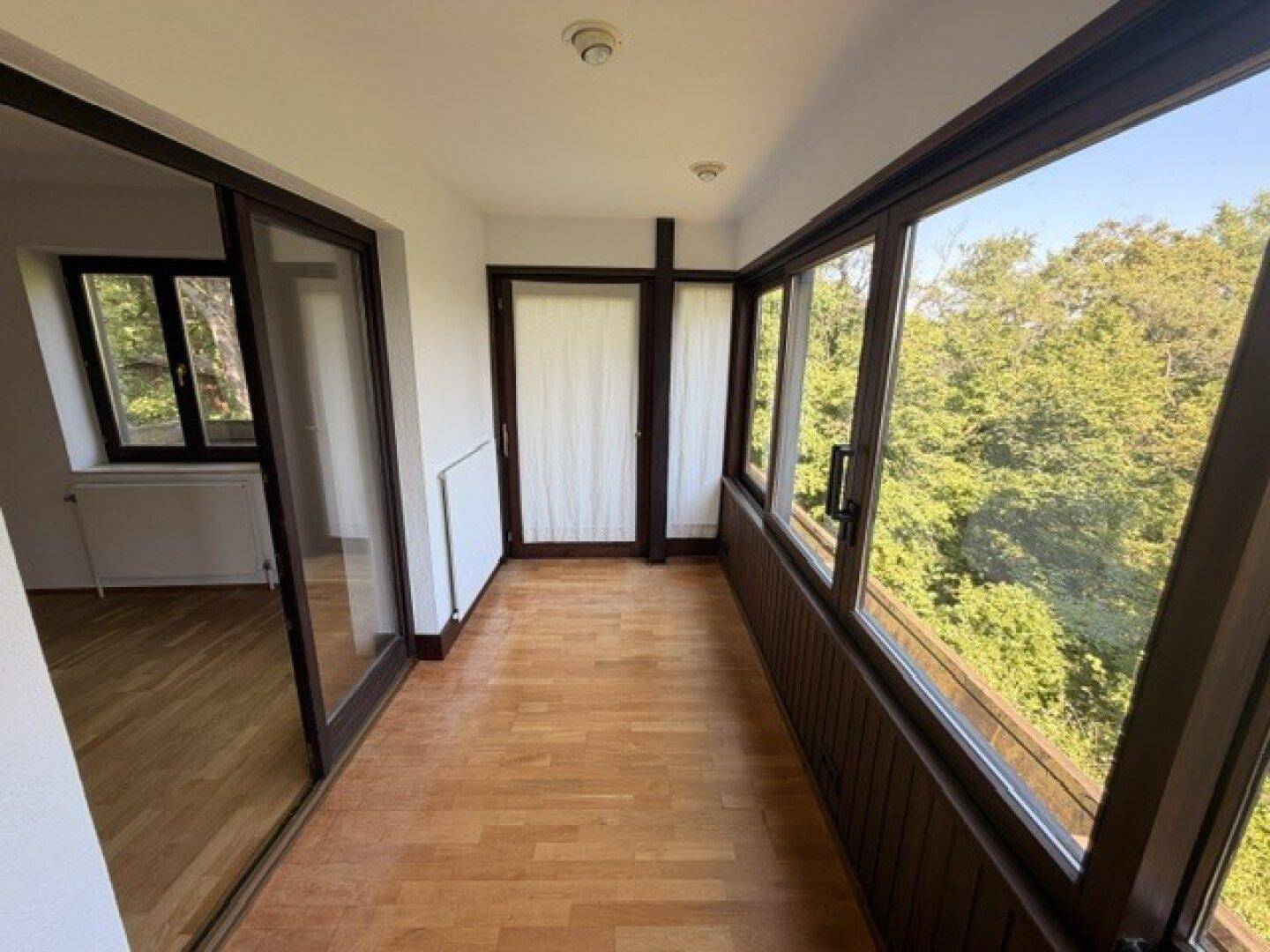 Verglaste Loggia mit Holzfußboden und großen Fenstern, die einen schönen Blick ins Grüne bieten.