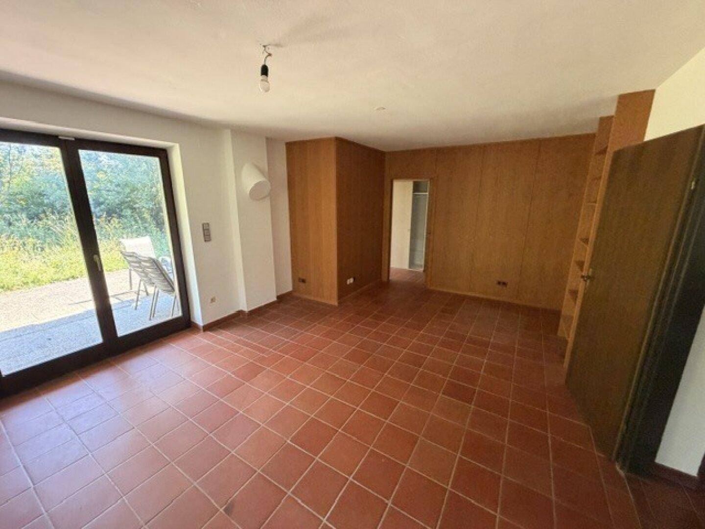 Helles Zimmer mit Terrakottafliesen und einer Holzwandverkleidung, die zur Terrasse führt.