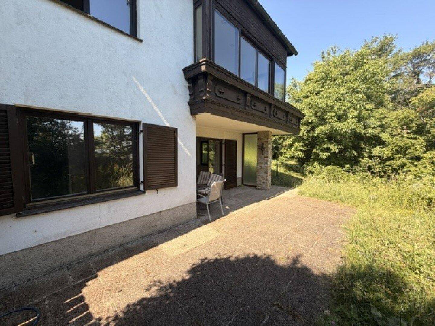 Außenansicht des Hauses mit einer gepflasterten Terrasse und einem darüberliegenden Balkon.