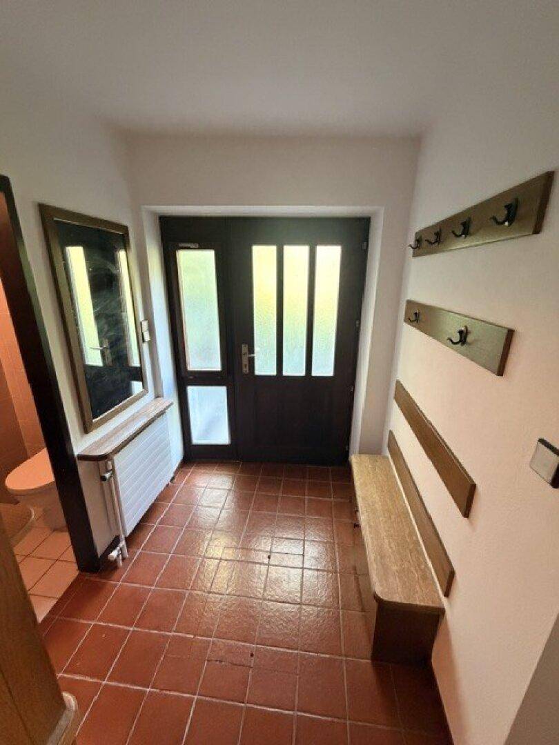 Eingangsbereich mit Terrakottafliesen, Garderobe und einer Holztür mit Glaseinsätzen.