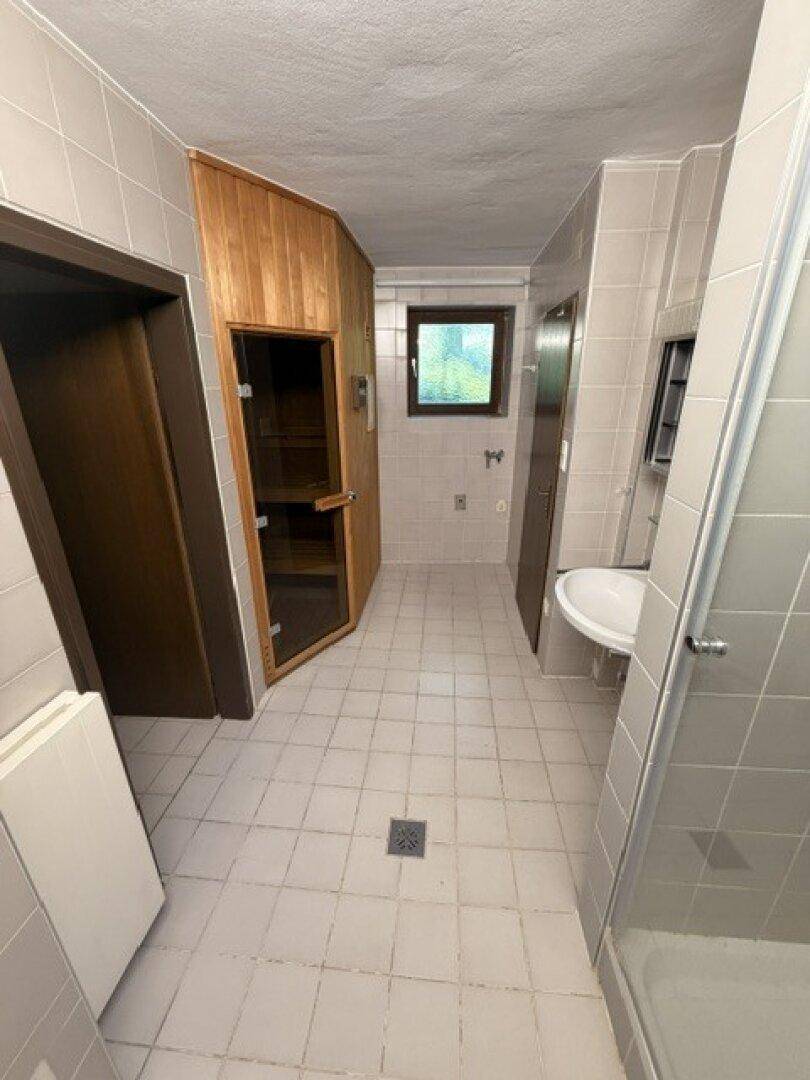 Badezimmer mit hellgrauen Fliesen, Duschkabine, Waschbecken und einer integrierten Sauna.