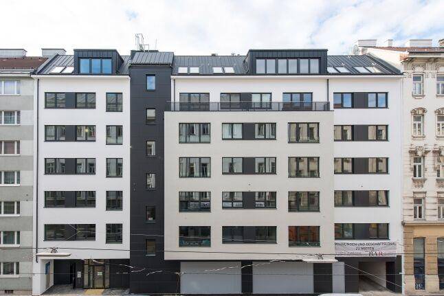 Moderne Wohnhausfassade mit Balkonen und großen Fenstern in urbaner Umgebung, ansprechend und zeitgemäß.