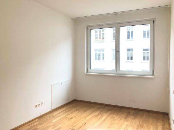 Helles Schlafzimmer mit Holzboden und einem großen Fenster, das den Raum gut belichtet und wohnlich macht.