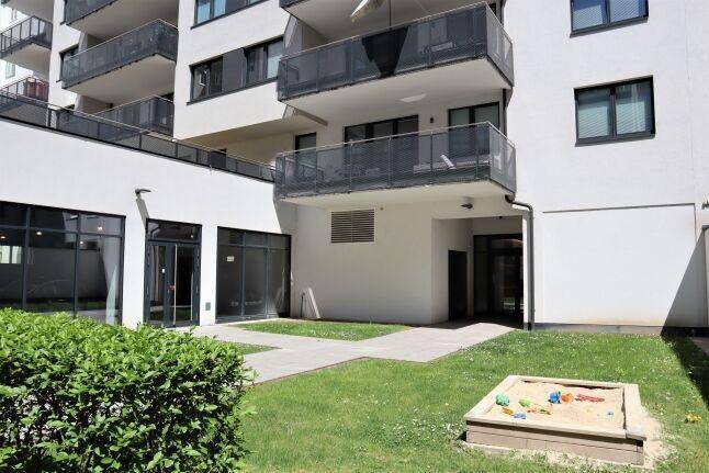 Gemeinschaftsgartenbereich mit Rasenfläche und Sandkasten, umgeben von modernen Gebäuden, ideal für Familien.