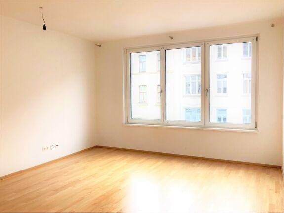 Geräumiger, heller Raum mit Holzboden und großen Fenstern, die eine angenehme Wohnatmosphäre schaffen.