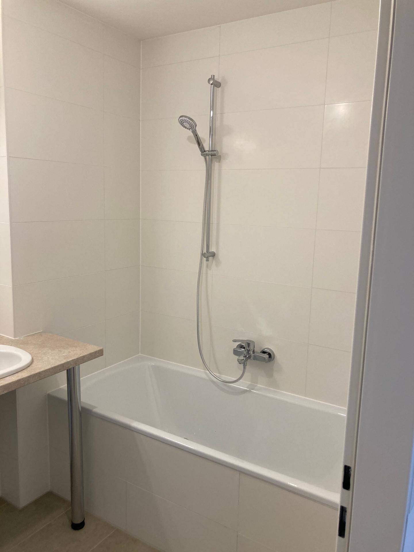 Badezimmer mit Badewanne und integrierter Dusche, gefliesten Wänden und hellem Ambiente.