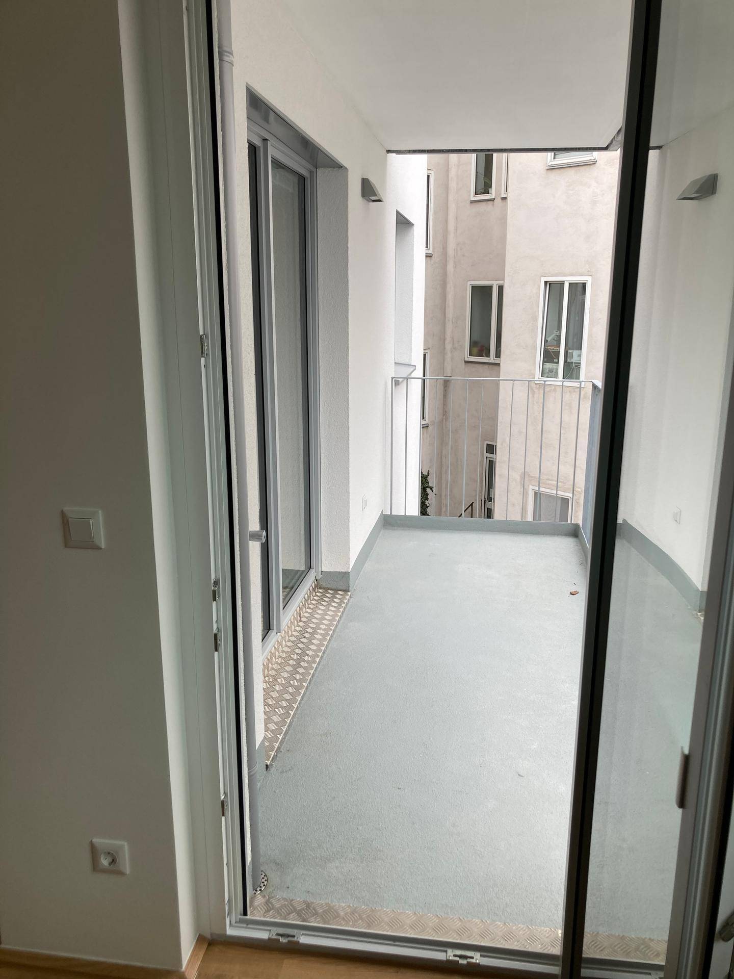Schmaler Balkon mit Metallgeländer und Blick auf die umliegenden Gebäude des Innenhofs.