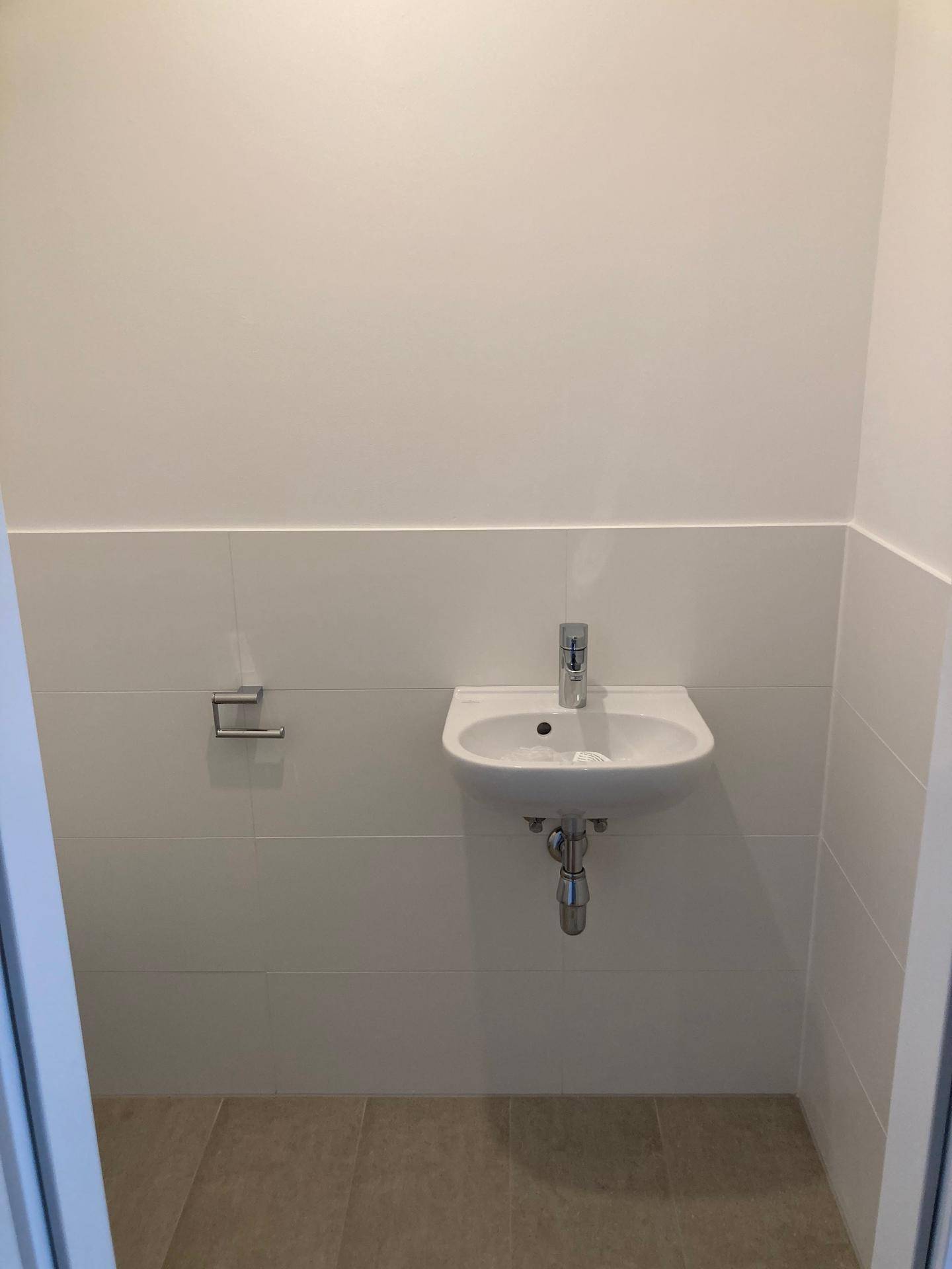 Kleines Gäste-WC mit Waschbecken und hellen Fliesen an den Wänden und auf dem Boden.