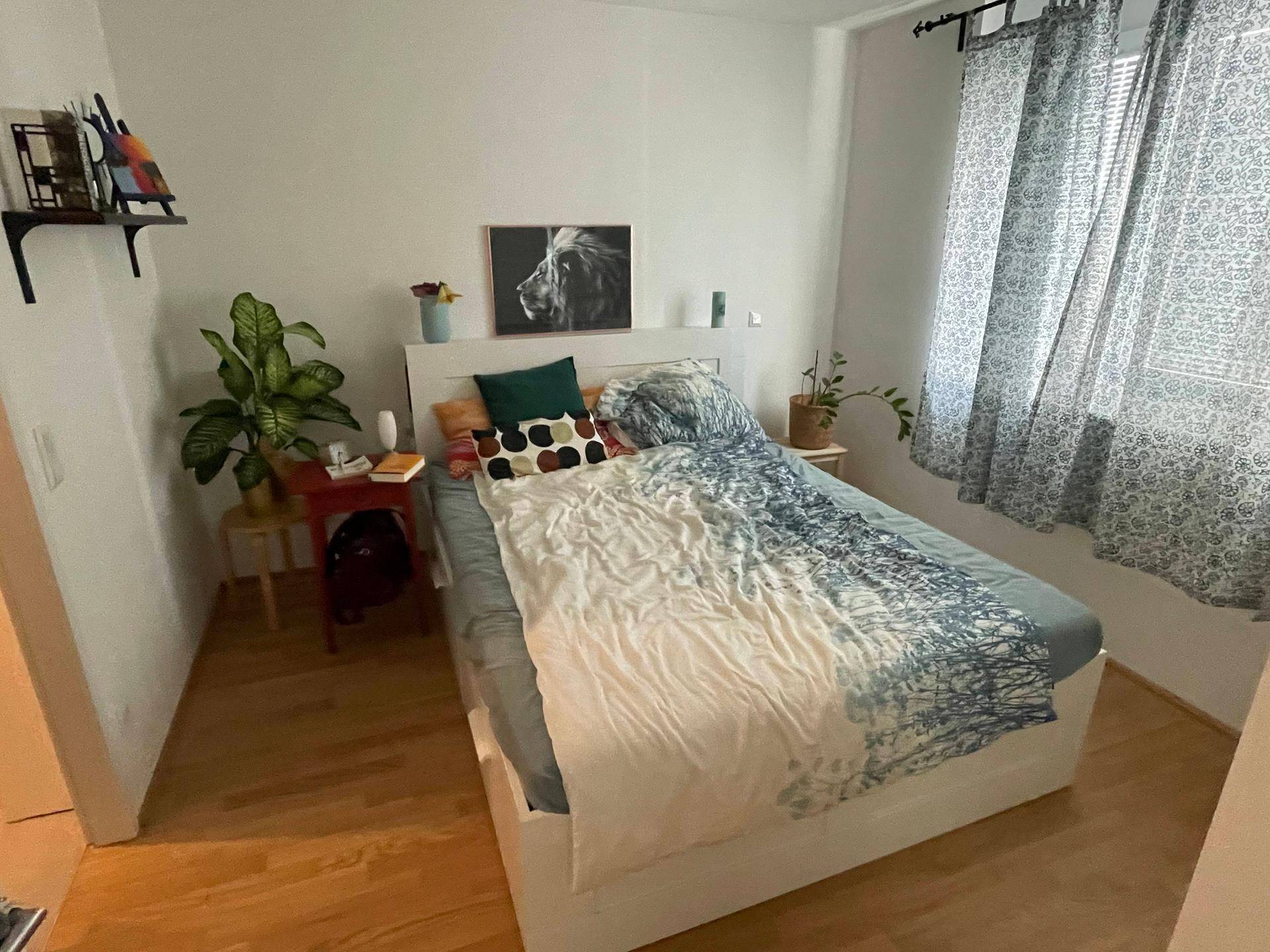 Helles Schlafzimmer mit Doppelbett, Holzboden und großem Fenster mit Vorhängen.