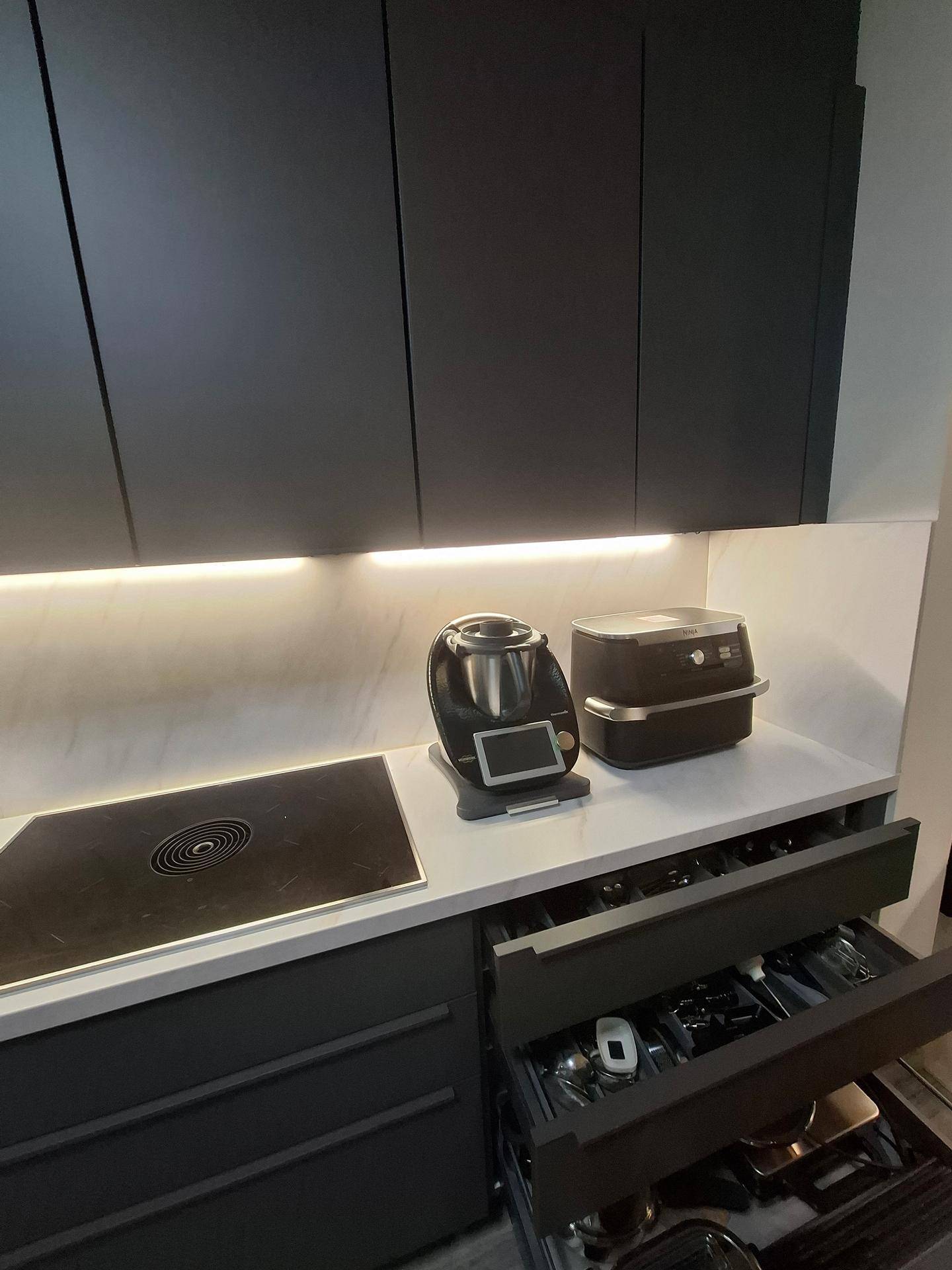 Moderne Küche mit Induktionskochfeld, Thermomix und gut organisierten Besteckschubladen.