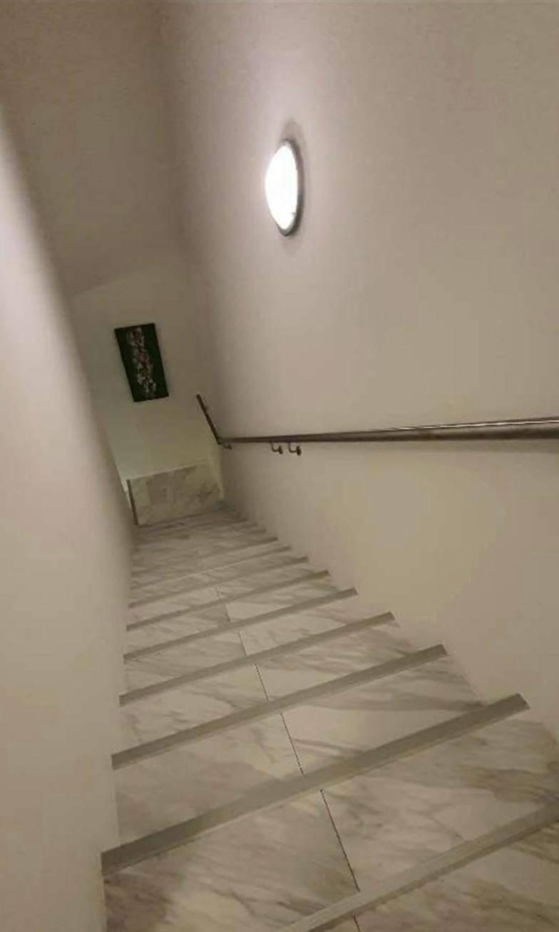 Helles Treppenhaus mit modernen Fliesenstufen und einem schlichten Handlauf.