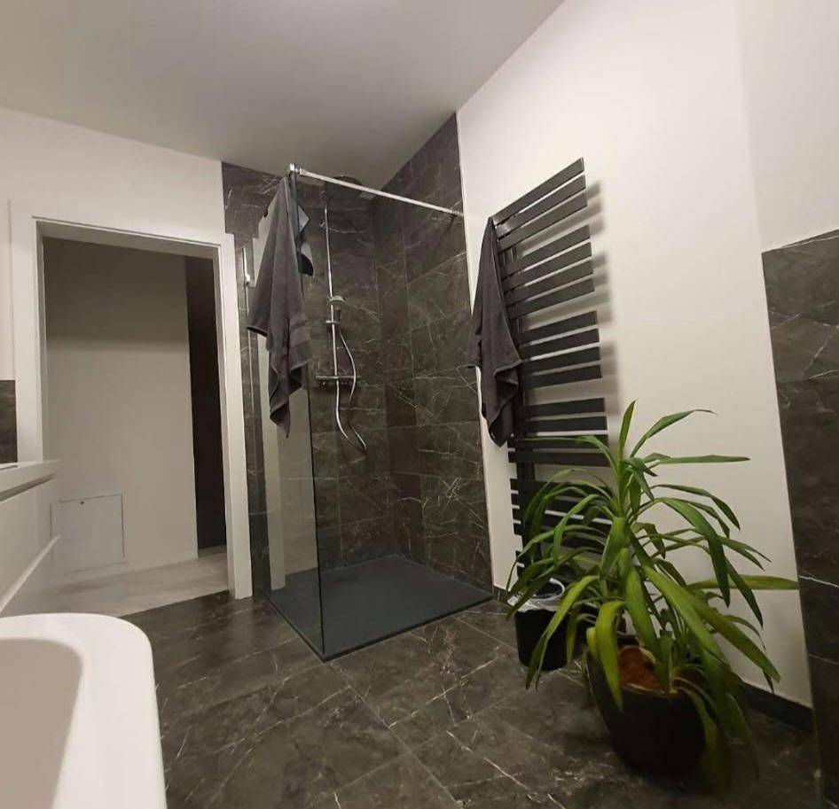 Elegantes Badezimmer mit begehbarer Dusche, beheiztem Handtuchhalter und dunklen Marmorfliesen.