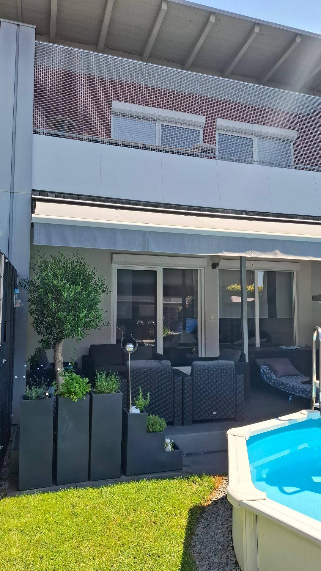 Gepflegte Terrasse mit Loungemöbeln, Rasenfläche und einem kleinen Aufstellpool.