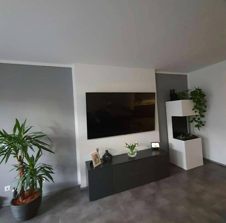 Heller Wohnraum mit wandmontiertem Fernseher, Sideboard und modernem Elektrokamin.