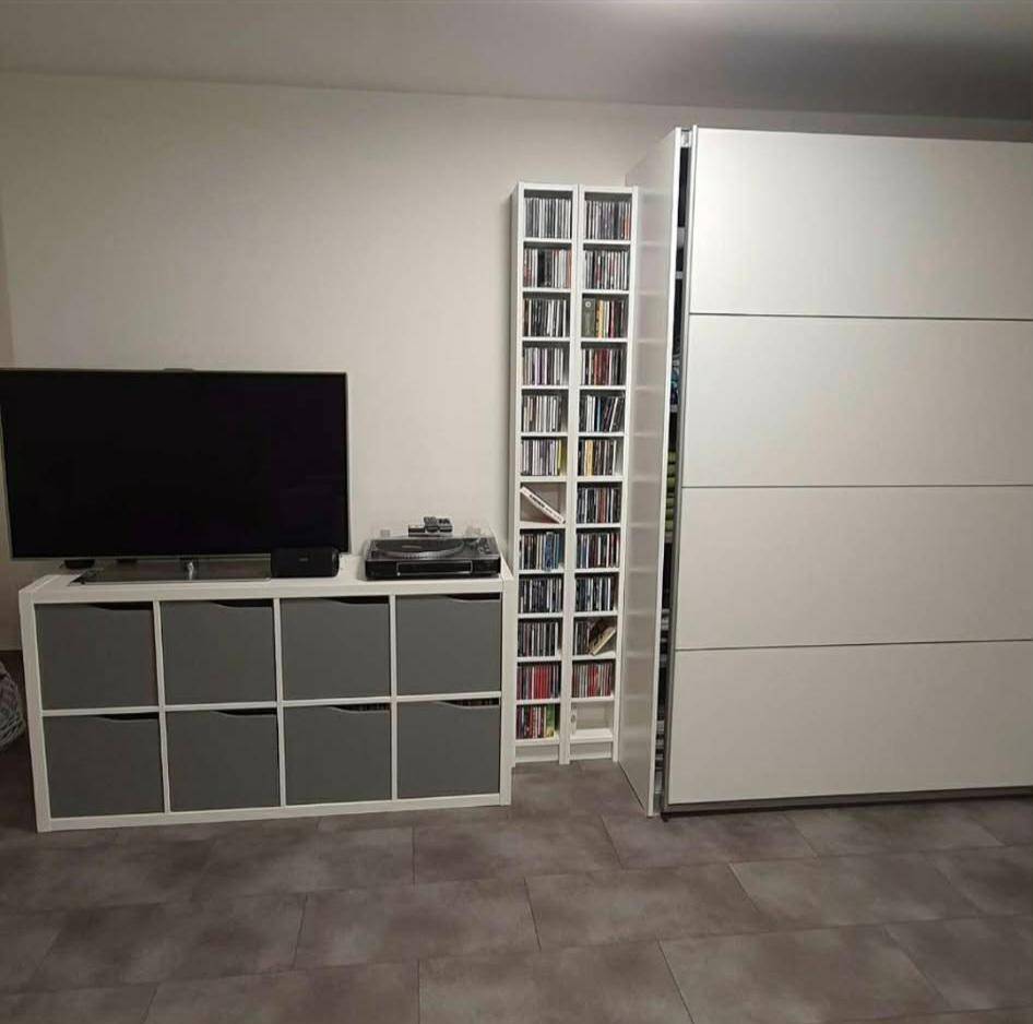 Raum mit Fernseher, Medienregal und großem weißen Kleiderschrank.