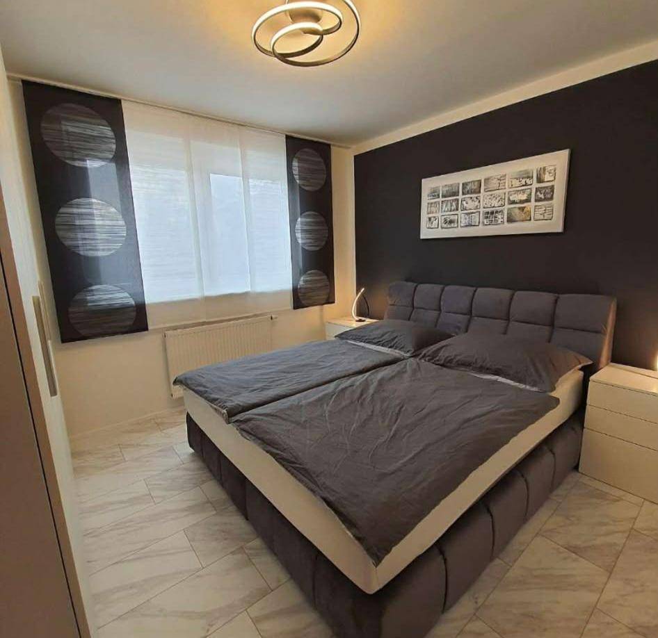 Gemütliches Schlafzimmer mit großem Bett, dunkler Akzentwand und hellen Fliesenboden.