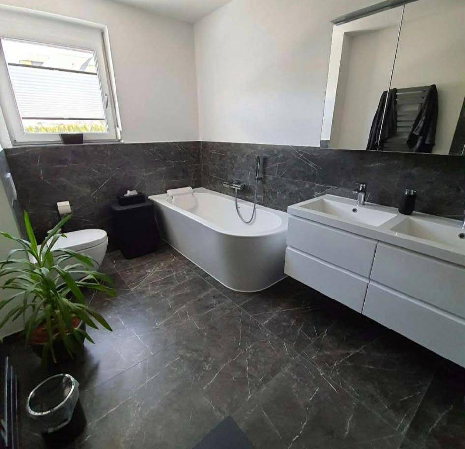 Modernes Badezimmer mit freistehender Badewanne, Doppelwaschbecken und dunklen Marmorfliesen.