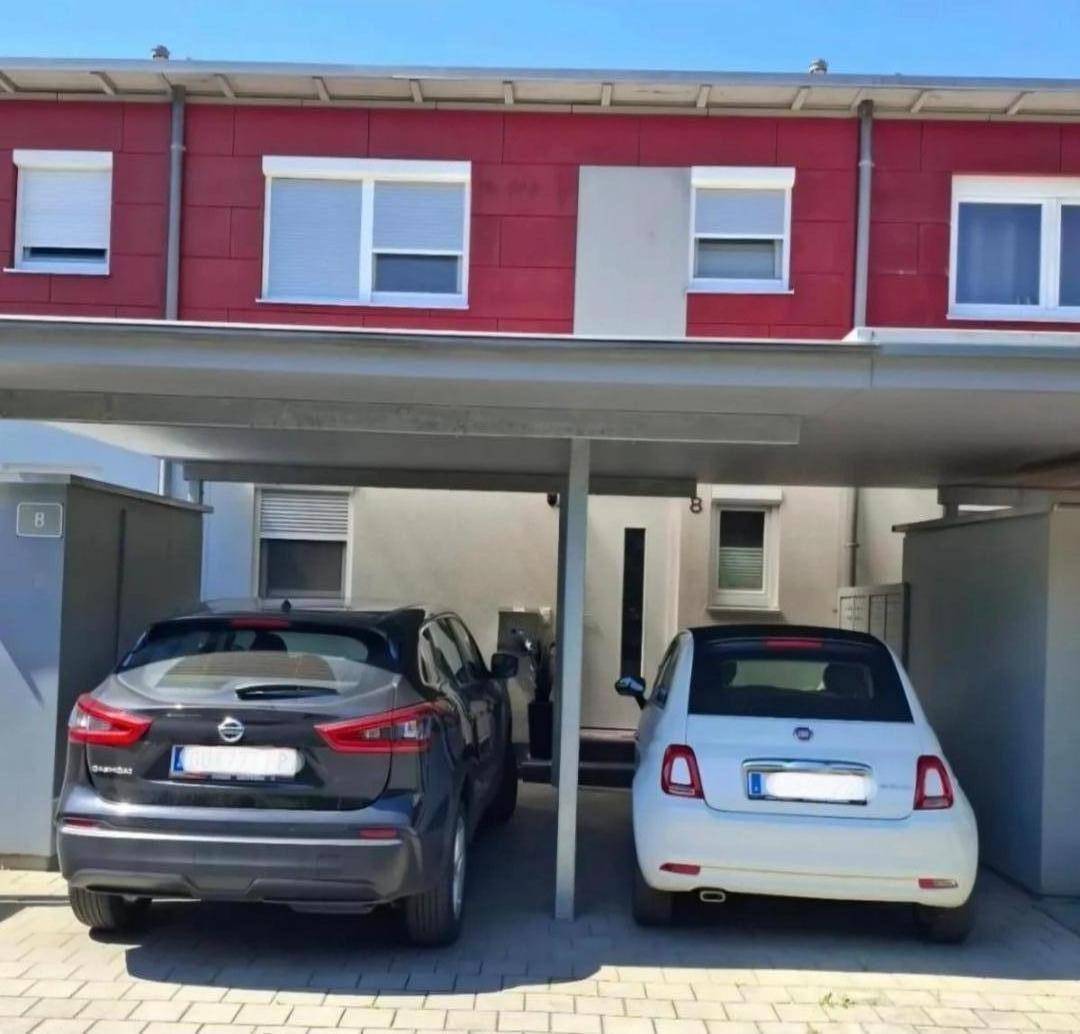 Moderne Gebäudefassade mit Carport und zwei geparkten Fahrzeugen davor.