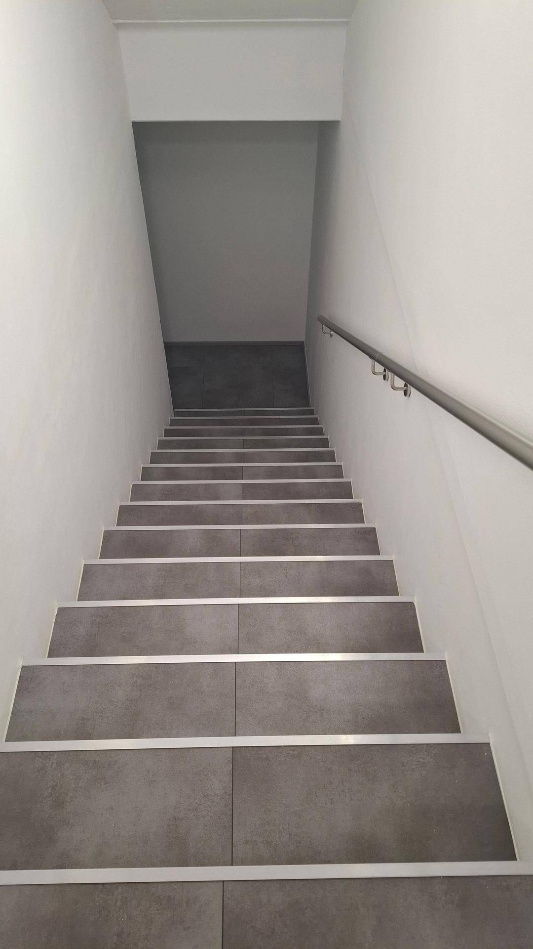 Modernes Treppenhaus mit dunkelgrauen Fliesenstufen und einem schlichten Handlauf.