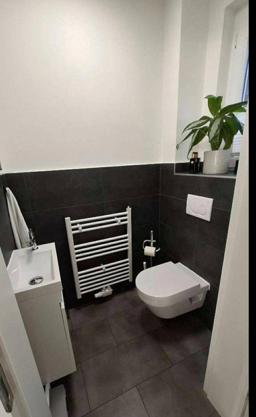 Modernes Gäste-WC mit wandhängendem WC, kleinem Waschbecken und beheiztem Handtuchhalter.
