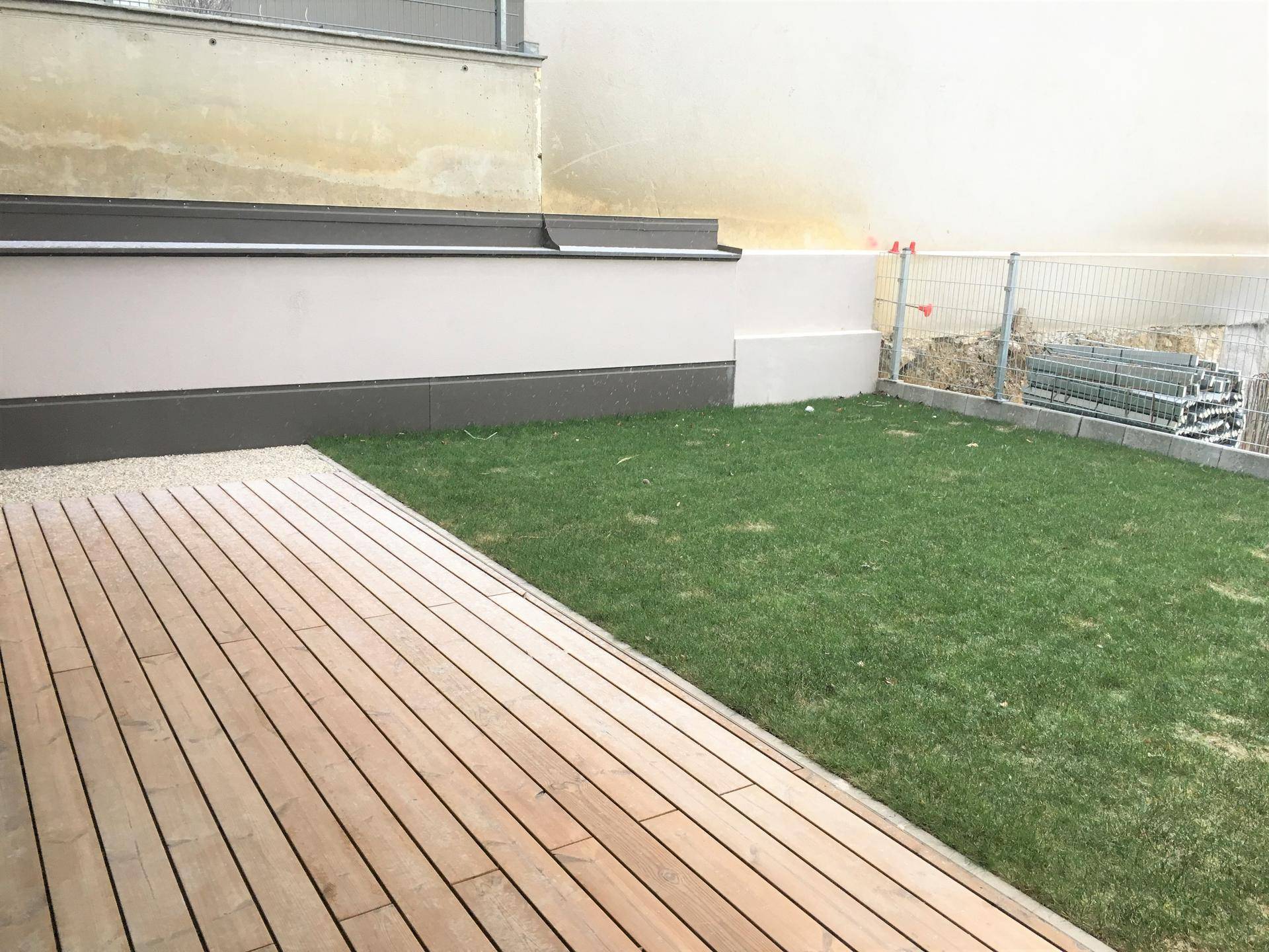 Privater Außenbereich mit Holzterrasse und Grünfläche, ideal für Entspannung im Freien am Neubau.