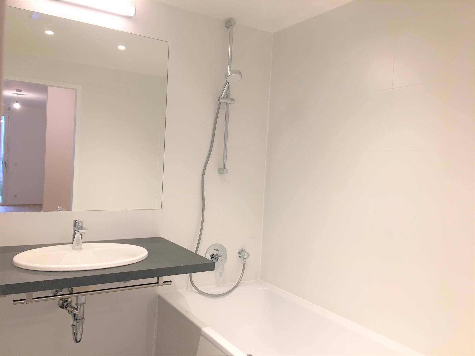 Helles Badezimmer mit Badewanne, integrierter Dusche und modernem Waschbecken unter einem großen Spiegel.