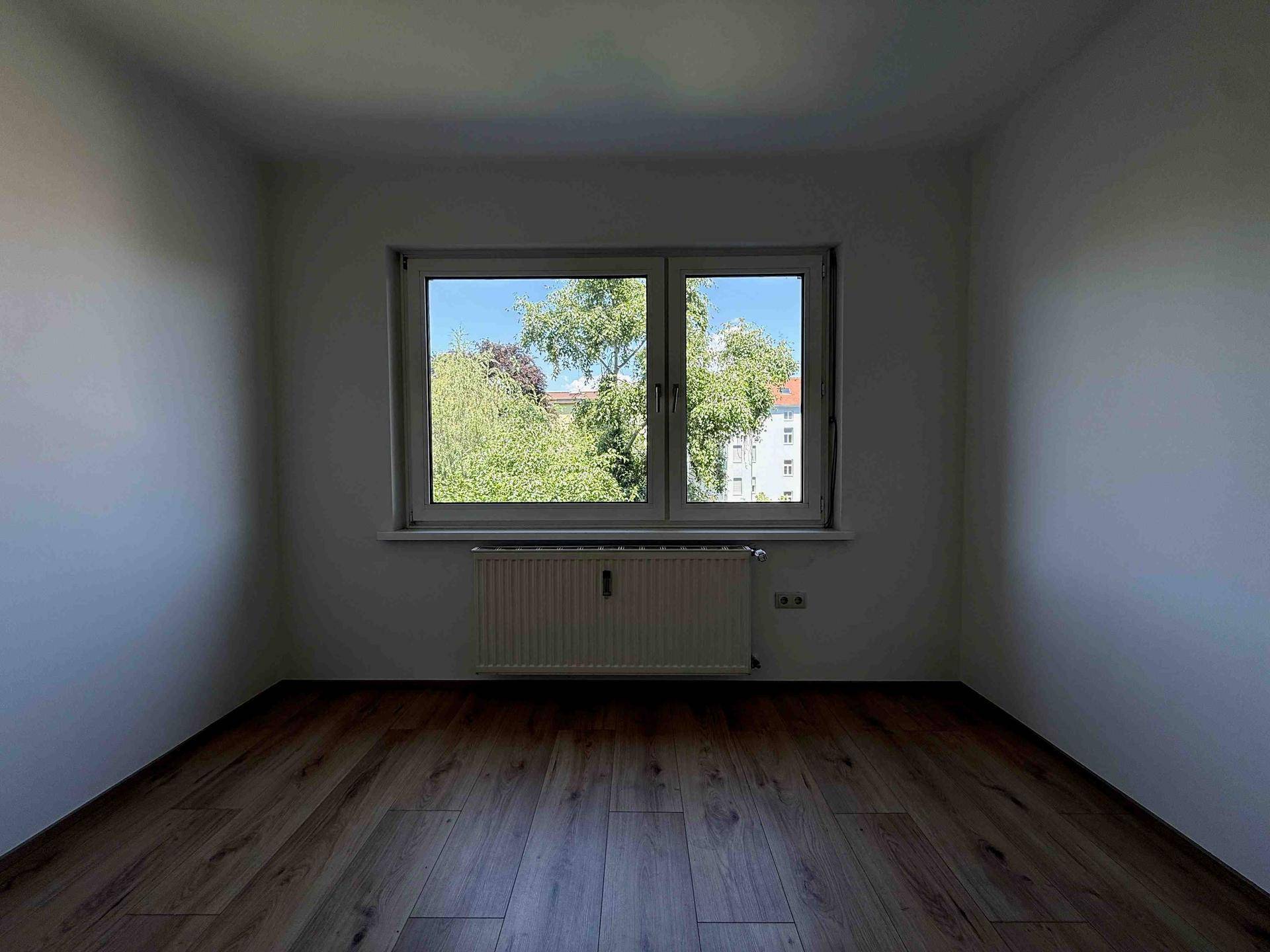 Heller Raum mit Laminatboden und großem Fenster, das einen grünen Ausblick bietet.