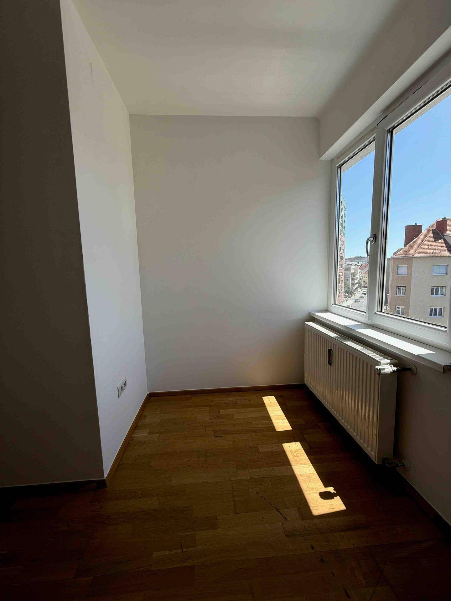 Sonniger Raum mit Parkettboden und Fenster, das viel natürliches Licht hereinlässt.