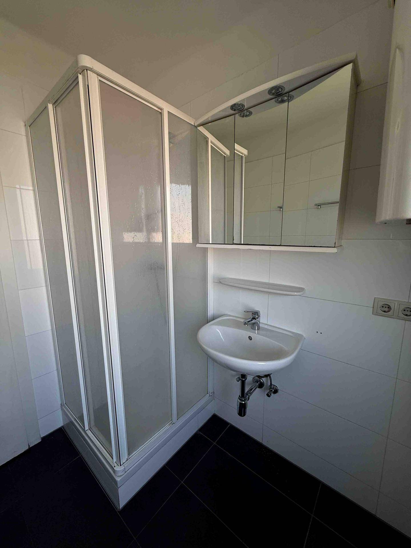 Funktionales Badezimmer mit Duschkabine, Waschbecken und Spiegelschrank, hell gefliest.