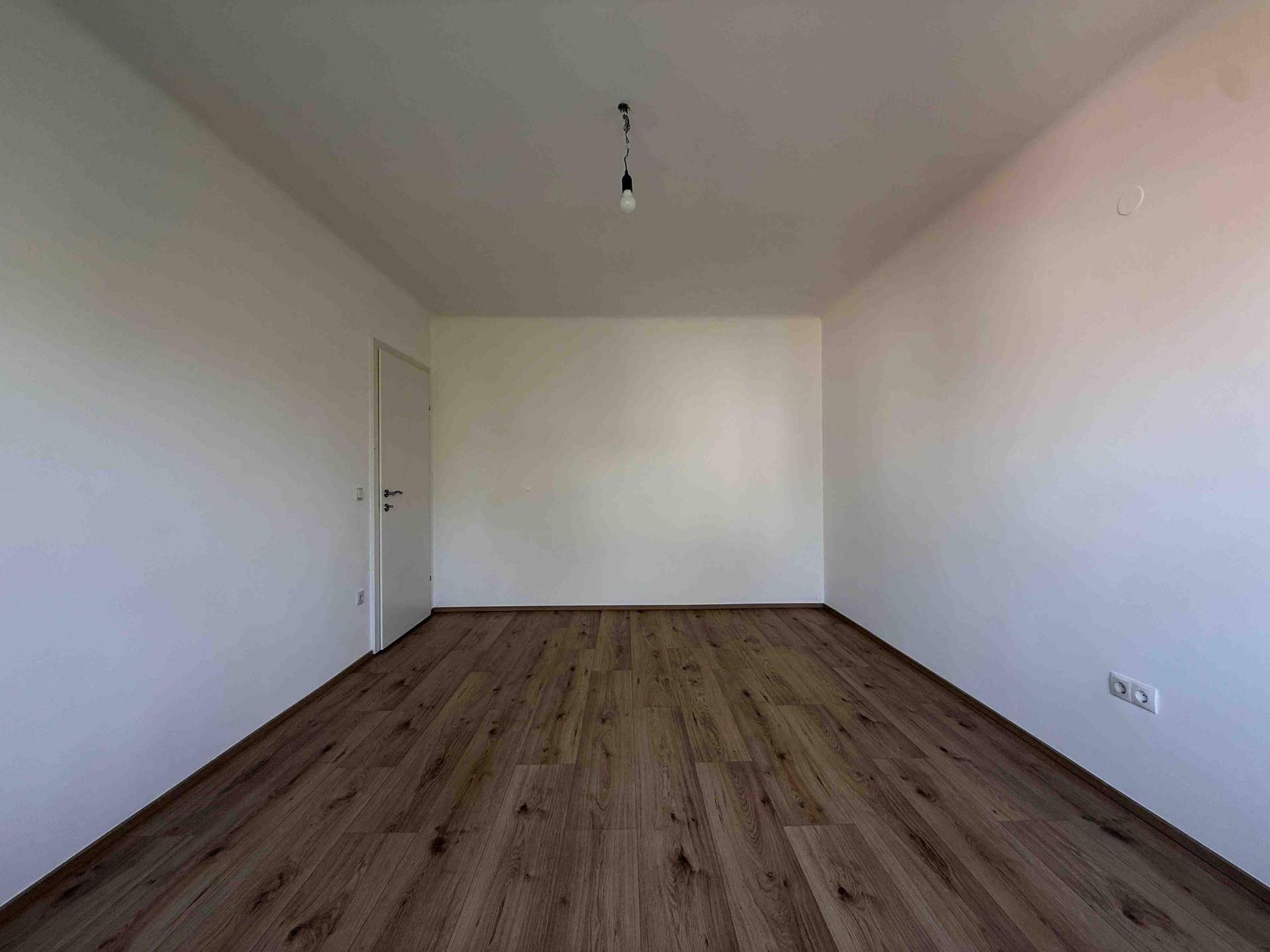Geräumiger, leerer Raum mit Laminatboden und weißen Wänden, bereit zur individuellen Gestaltung.