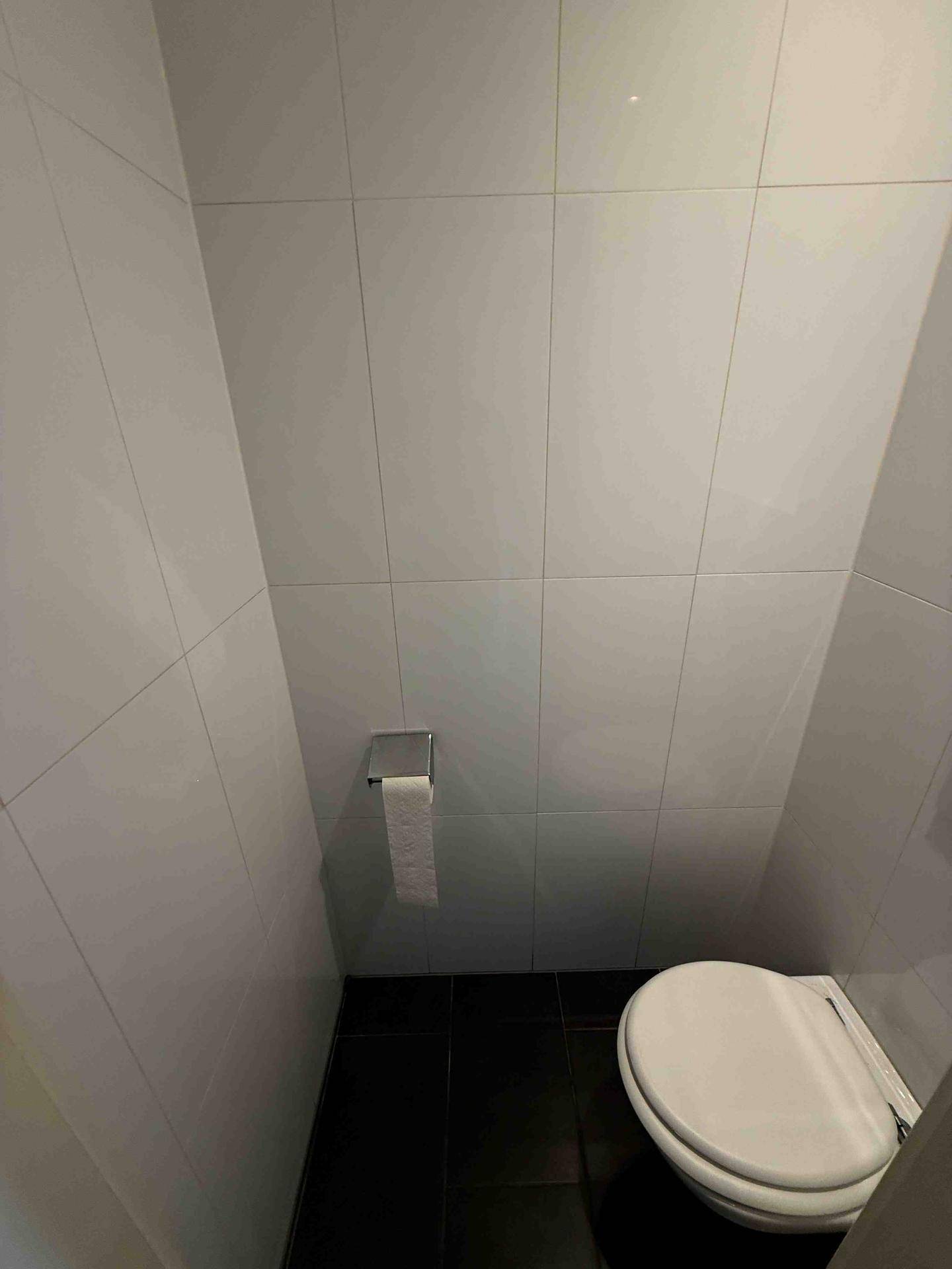 Separates WC mit Wandfliesen und dunklem Boden, ausgestattet mit einer modernen Toilette.